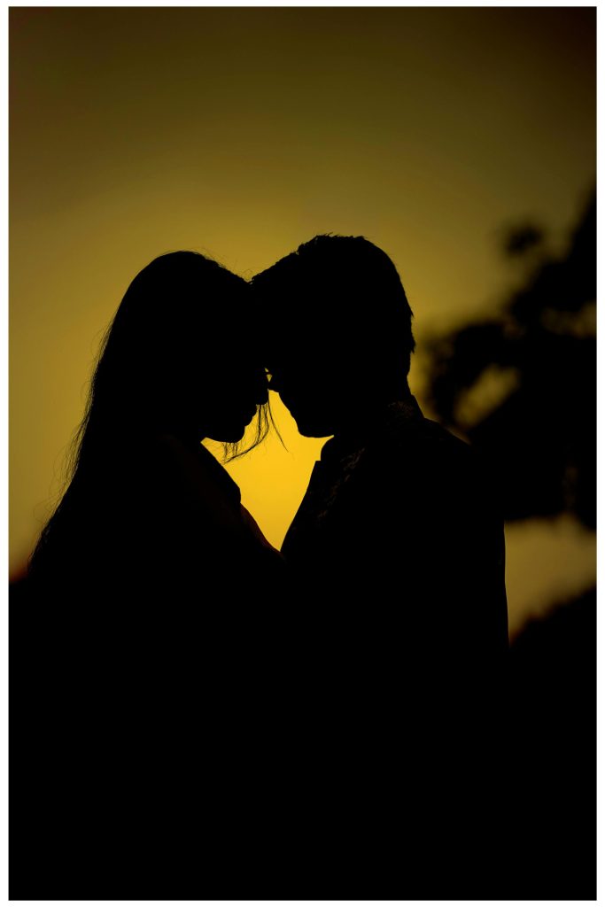 Die Silhouette eines verliebten Paares vor einem warmen Sonnenuntergangshimmel – ein Ausdruck von Romantik.